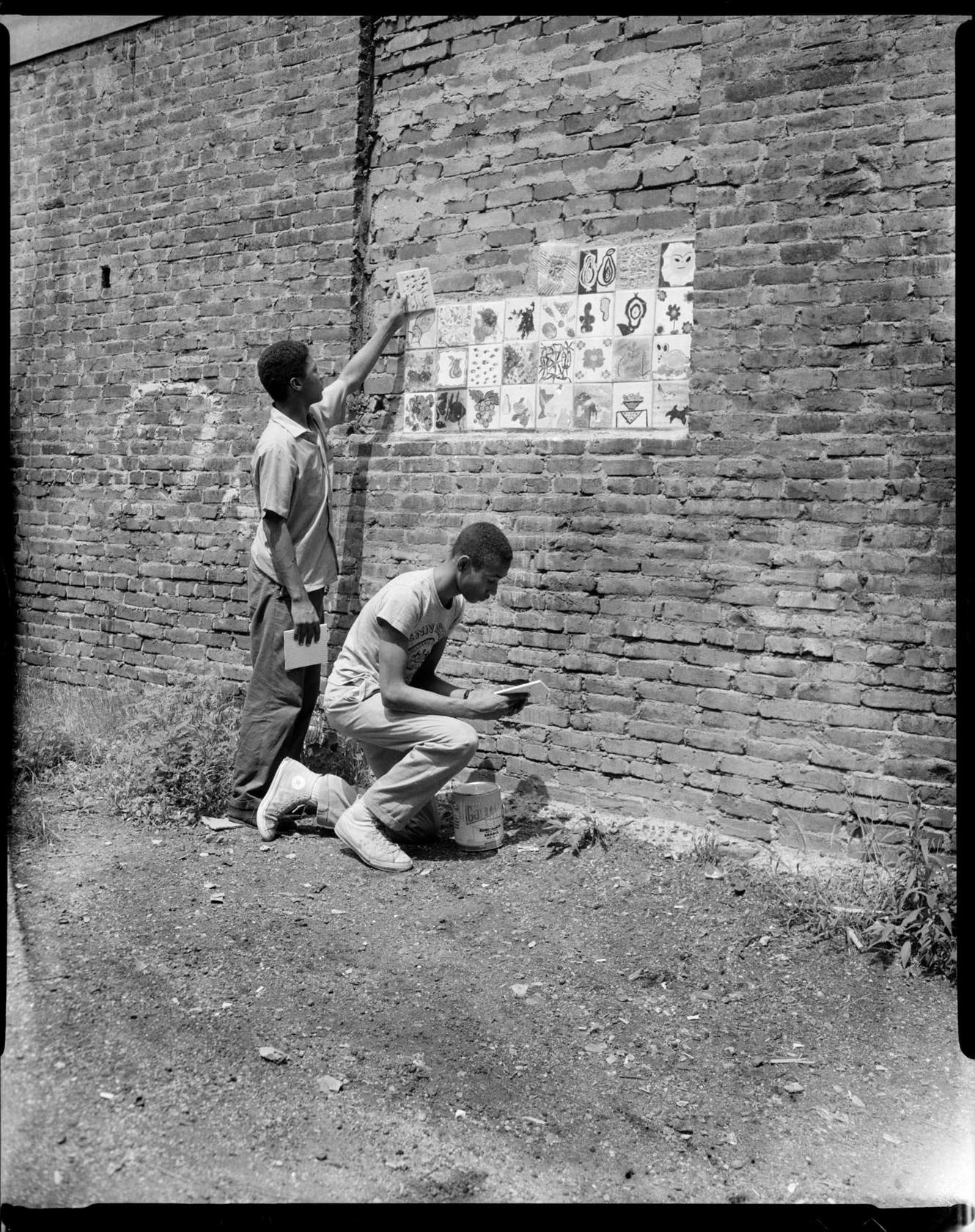 Two Young Men Adhering Decorative Tiles To Brick Wall Outdoors CMOA