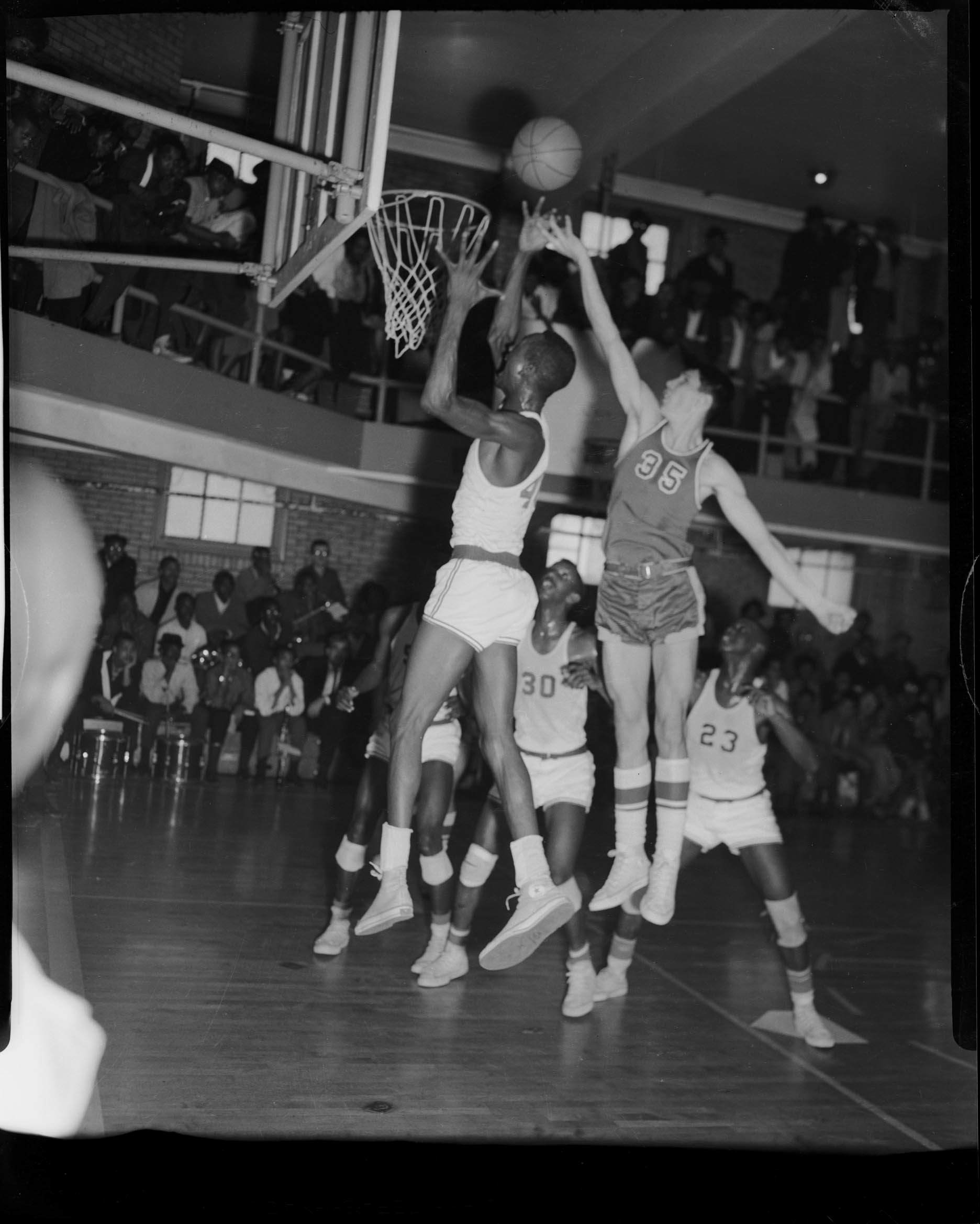 Two basketball players leaping for the ball in game in gymnasium with