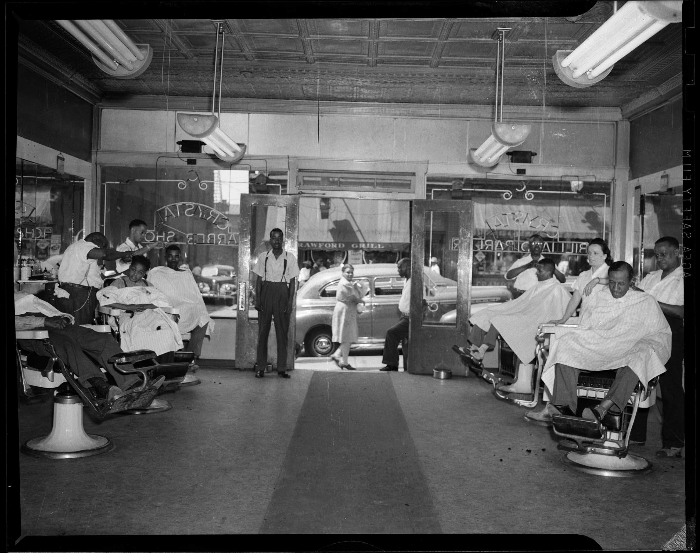 Barbers at work in the Crystal Barber Shop with view of Crawford Grill No. 1 through front door