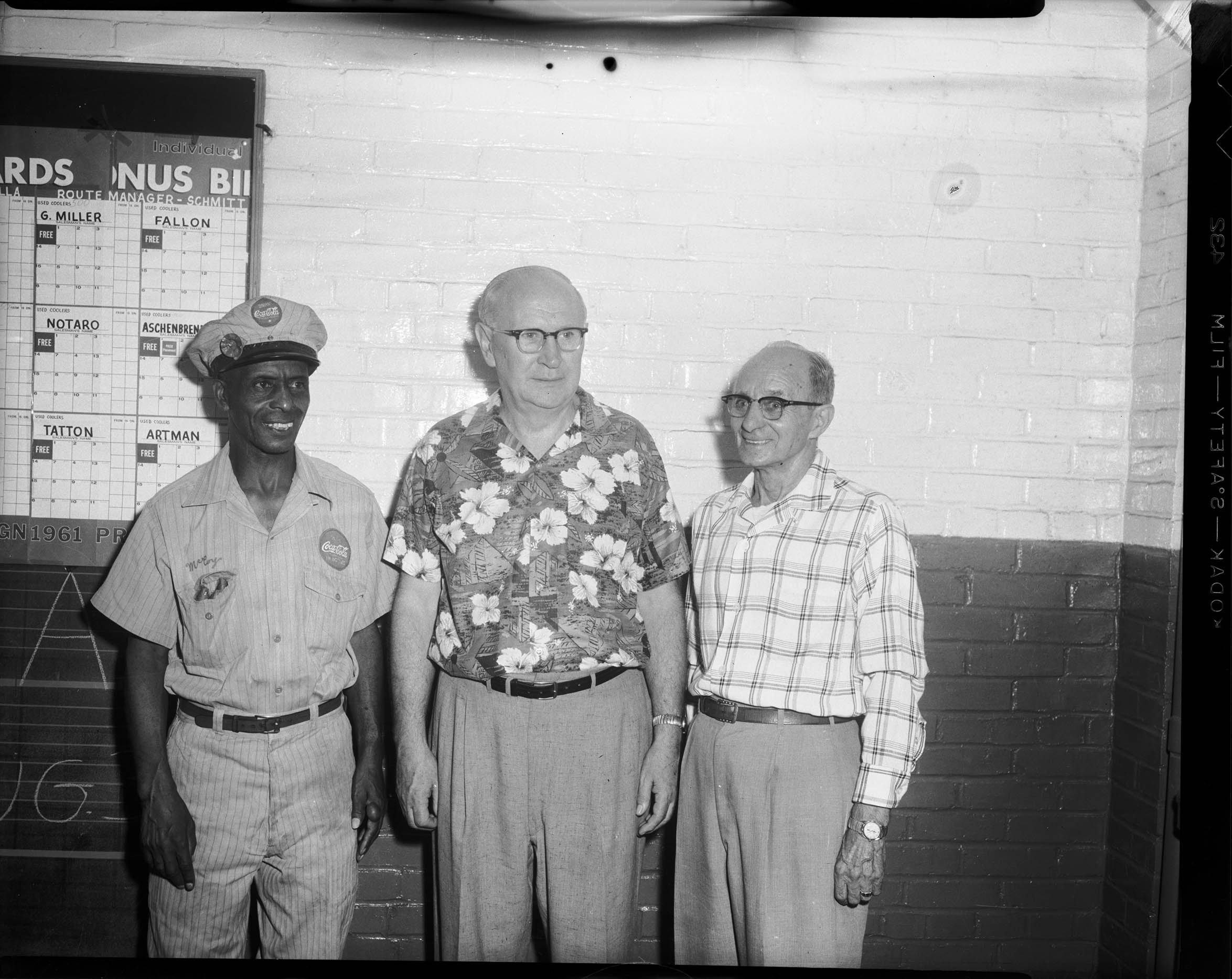 Man wearing CocaCola uniform standing with two men, one wearing