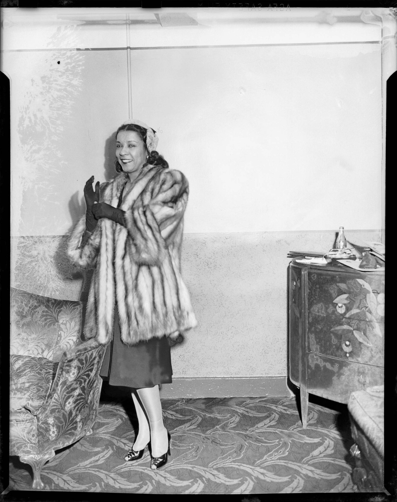 Gladys Hampton wearing dark gloves and fur coat, standing in between