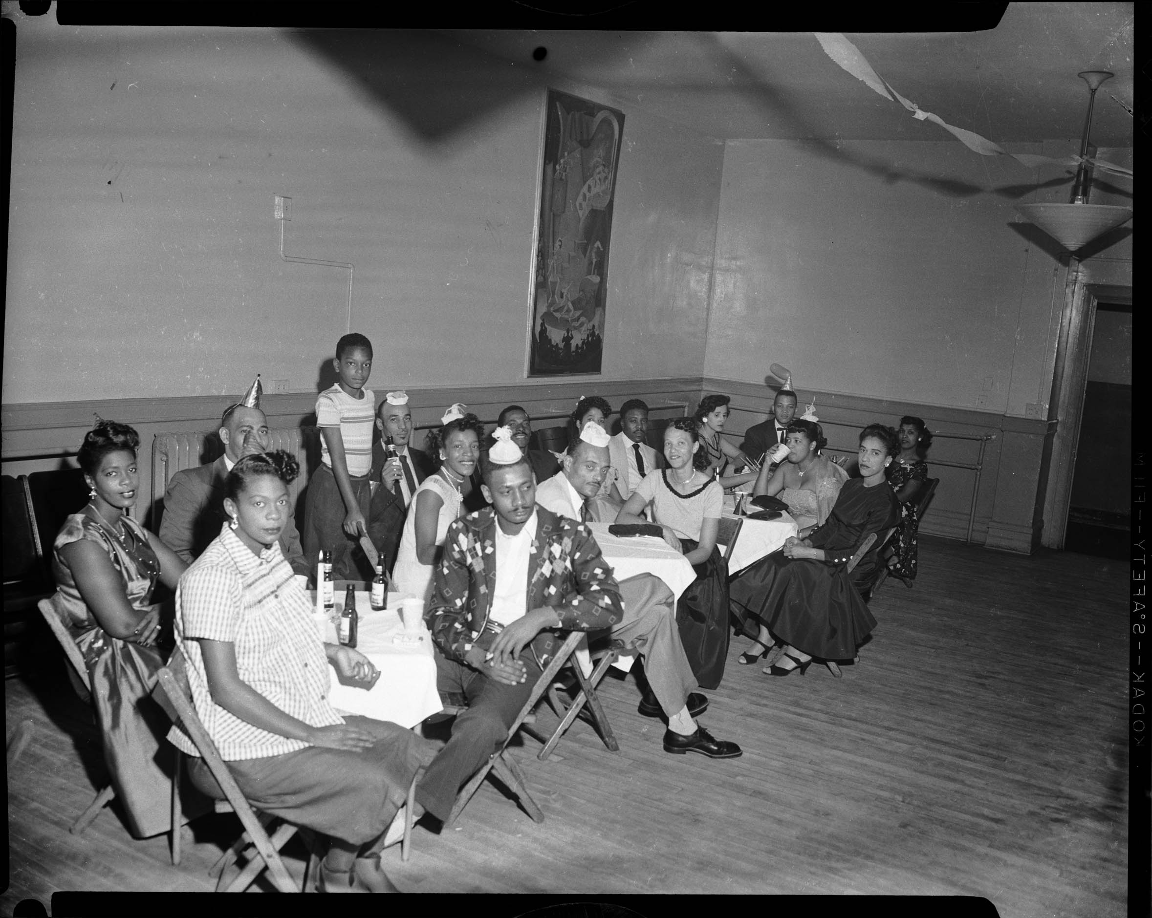 Men And Women Seated On Folding Chairs In Room Decorated With