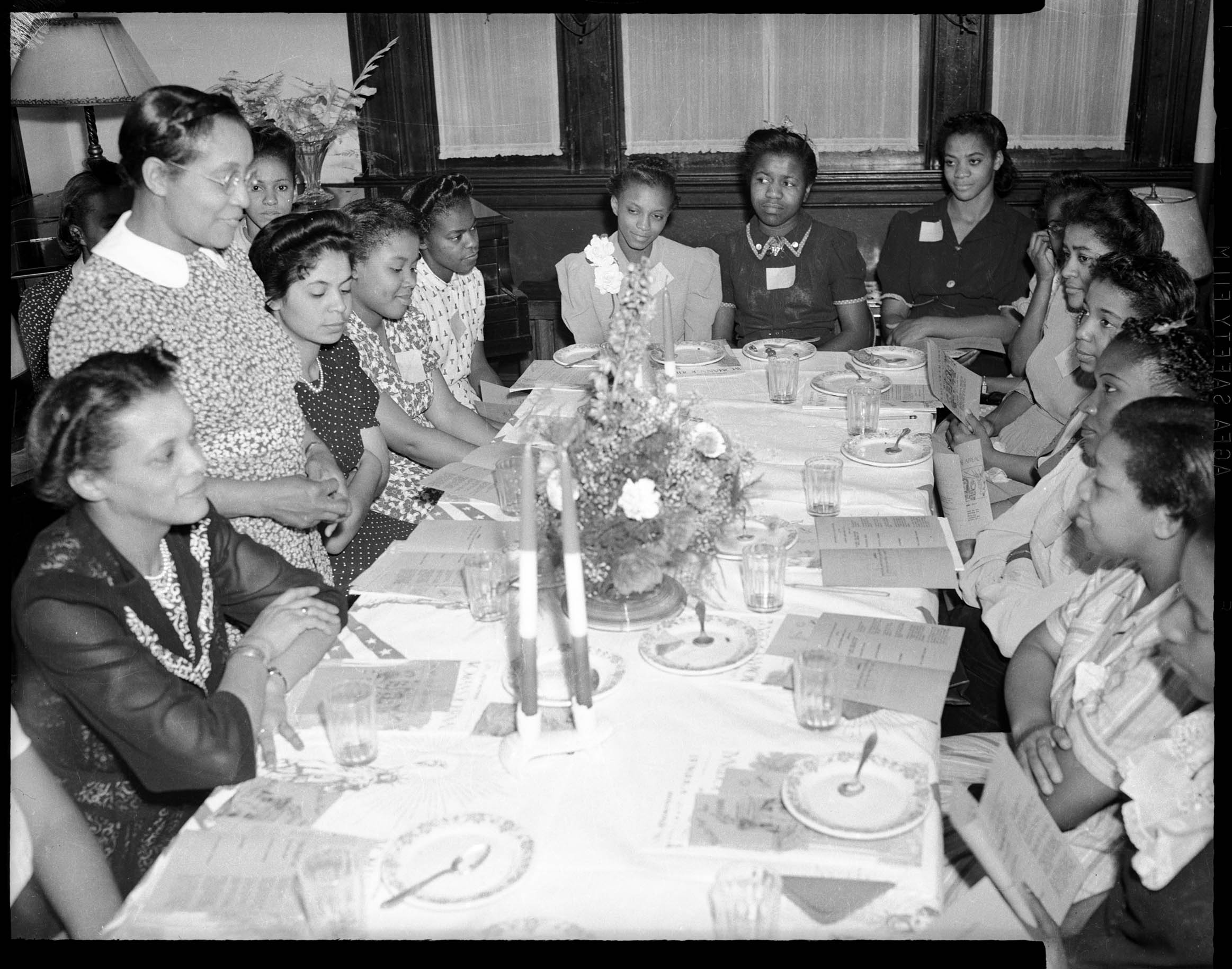 Fourteen women, including three women wearing name tags, seated around