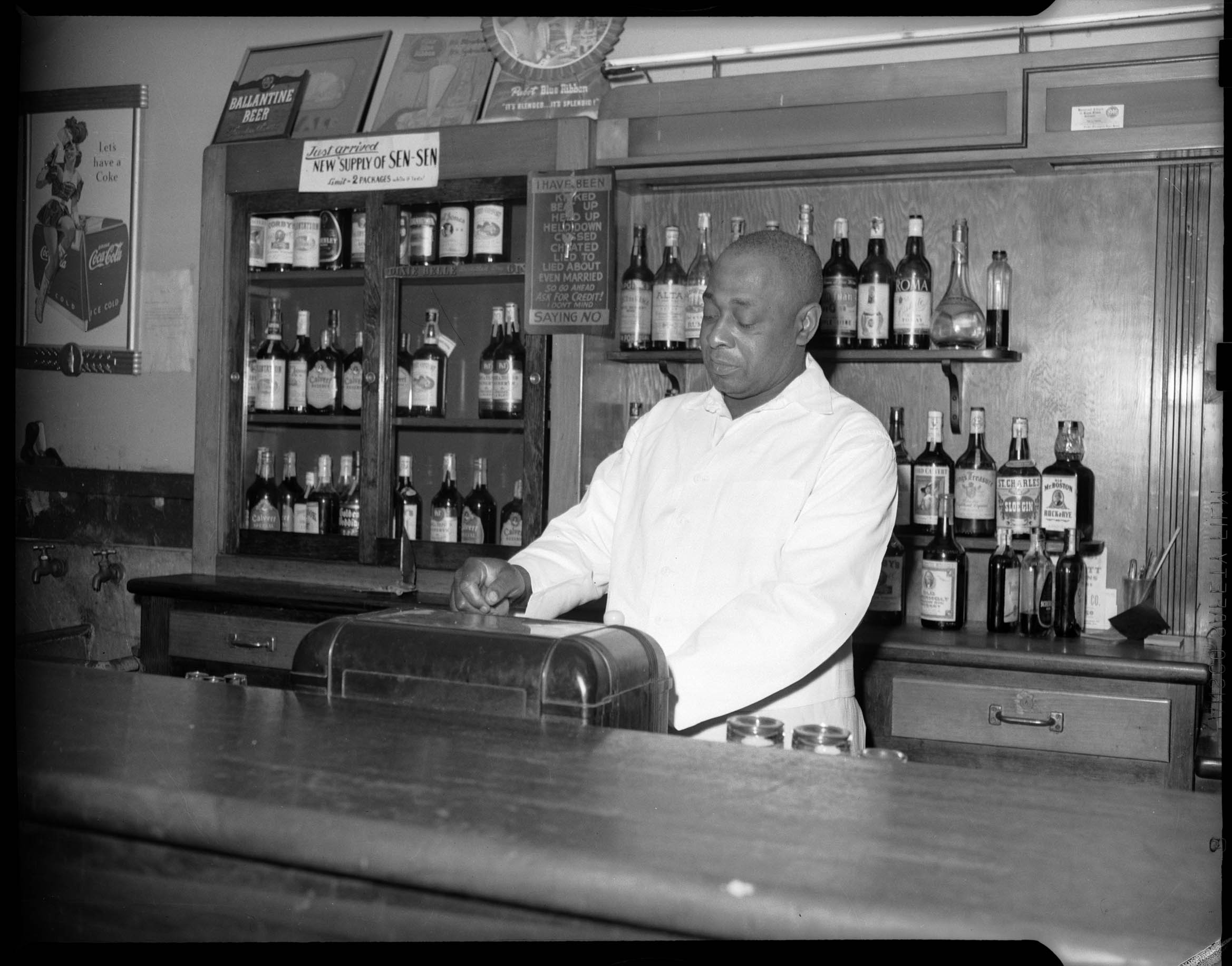 Bartender George Moore Behind Bar With Advertisements For Ballantine Pabst And Coca Cola And Sign Reading I Have Been Kicked Beat Up Held Up Held Down Crossed Cheated Lied To Lied About Even