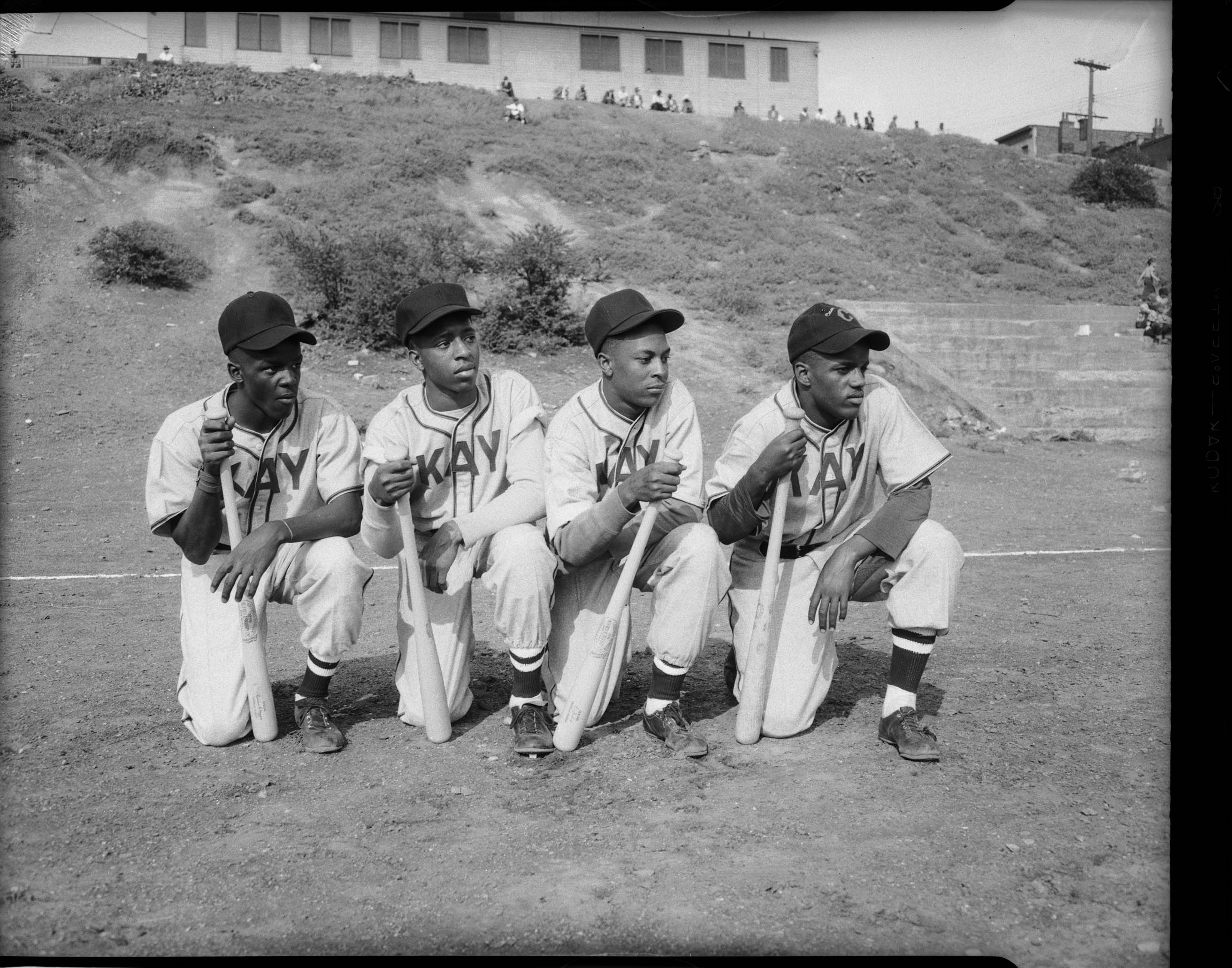 Group portrait of four young men wearing light colored baseball