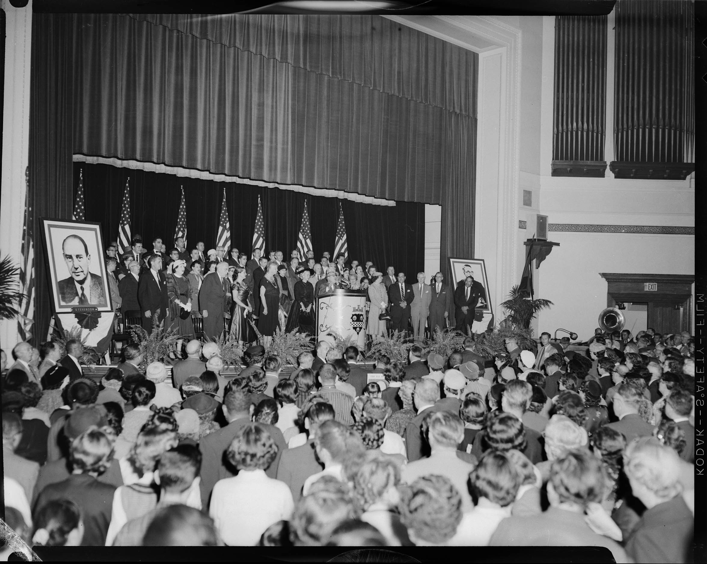 Audience standing before women and men on stage, including Joseph S